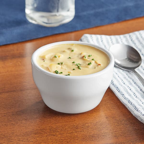 A white bouillon cup of soup with a spoon on a table.