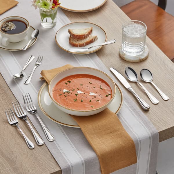 A table set with a bowl of soup, a glass of water, and an Acopa Edgeworth stainless steel fork.
