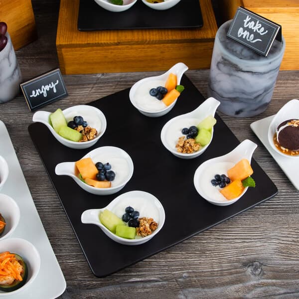A tray of fruit, yogurt, and nuts on Acopa Matte Black stoneware plates.
