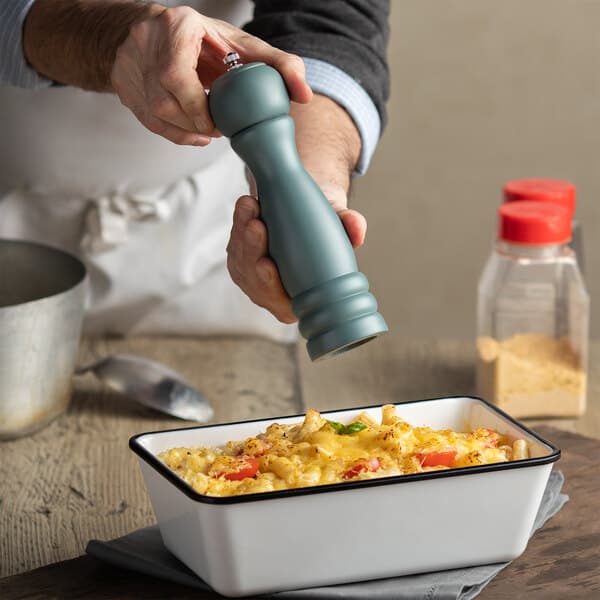 A person using an Acopa steel blue wooden pepper mill to season food.