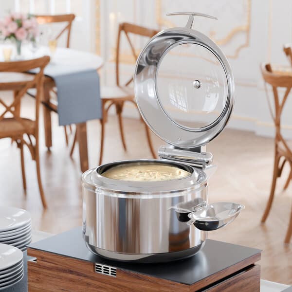 An Acopa stainless steel soup chafer with an open glass lid on a table.