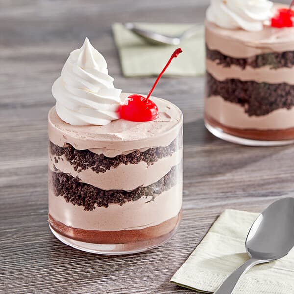 An Acopa glass bowl filled with a dessert topped with whipped cream and a cherry, with a spoon on a napkin.