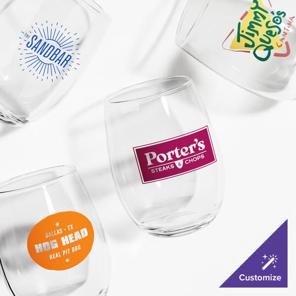 A group of Acopa customizable stemless wine glasses with different logos on a table.