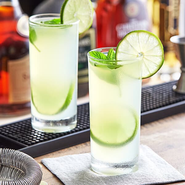 Two Acopa Collins glasses with drinks and lime slices on a napkin.