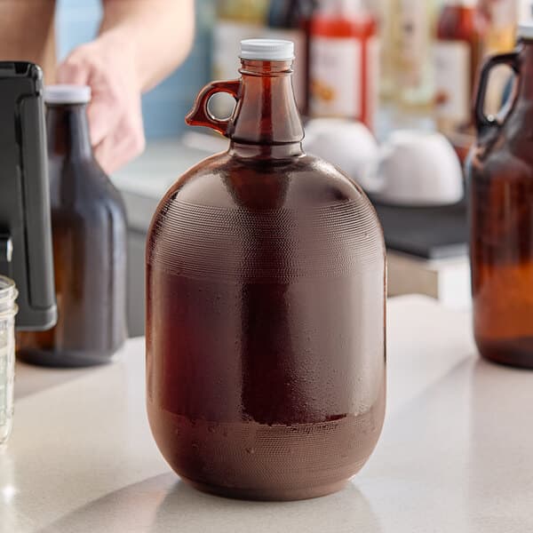 A hand pouring beer from a brown Acopa growler into a glass on a table.
