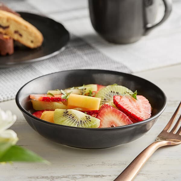 An Acopa Condesa scalloped porcelain bowl filled with fruit on a table with a fork.