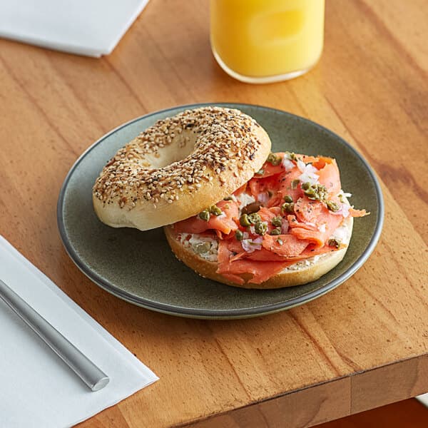 An Acopa Embers moss green matte coupe stoneware plate with a bagel sandwich on it.