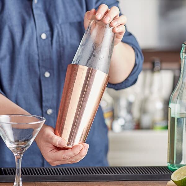 A woman using an Acopa copper cocktail shaker to pour a drink into a glass.
