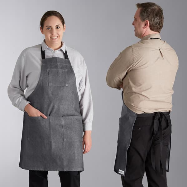 A man and woman wearing Acopa grey denim bib aprons with black webbing.
