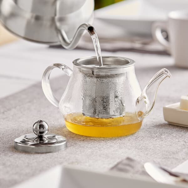 a teapot with a metal kettle pouring liquid into it