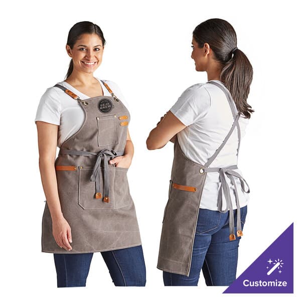 A woman wearing a customized Acopa Hazleton canvas cross-back bib apron with three pockets on a counter in a professional kitchen.