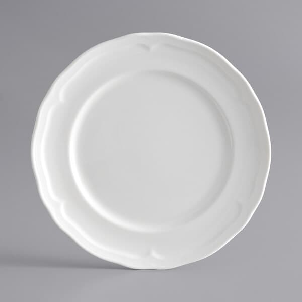 An Acopa Condesa porcelain plate with a decorative scalloped edge on a gray background.