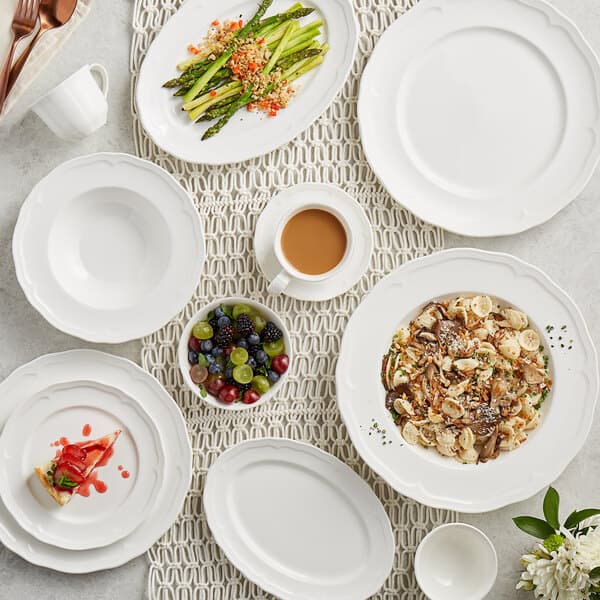A table with Acopa Condesa pearl white plates, bowls, and cups on it.