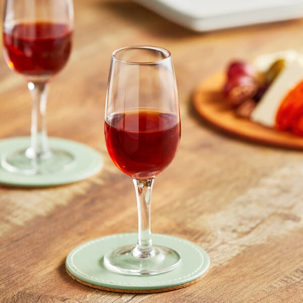 An Acopa Select sherry glass filled with red liquid on a wooden coaster on a table.