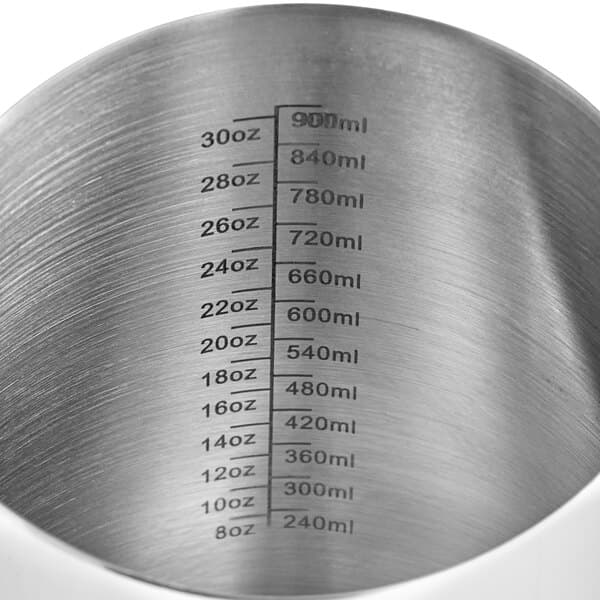 An Acopa stainless steel frothing pitcher with measuring lines on a counter.