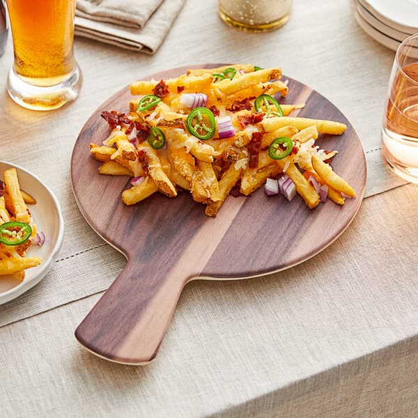An Acopa faux wood melamine serving board with fries and jalapenos on it on a table with a glass of beer.