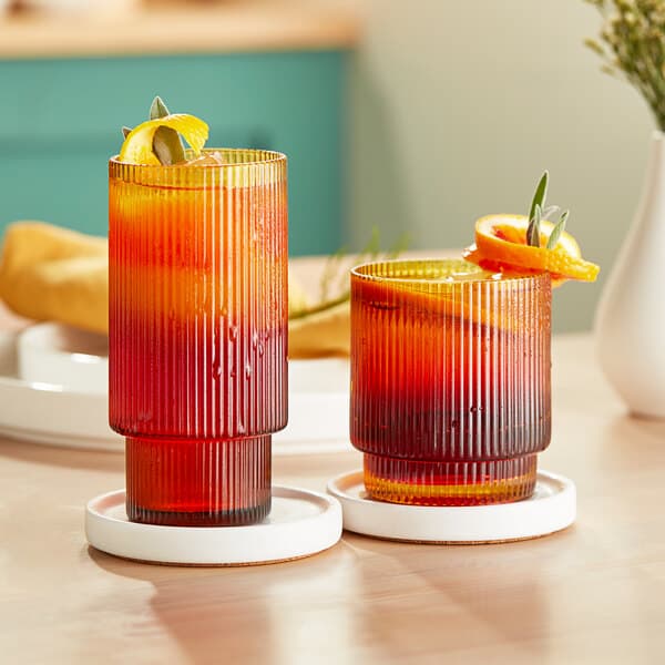 Two Acopa Lore amber glasses with orange and brown drinks on a table.