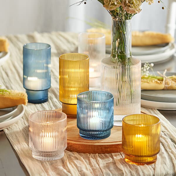 A table with a group of Acopa Lore amber glass tealight holders and flowers on a table.