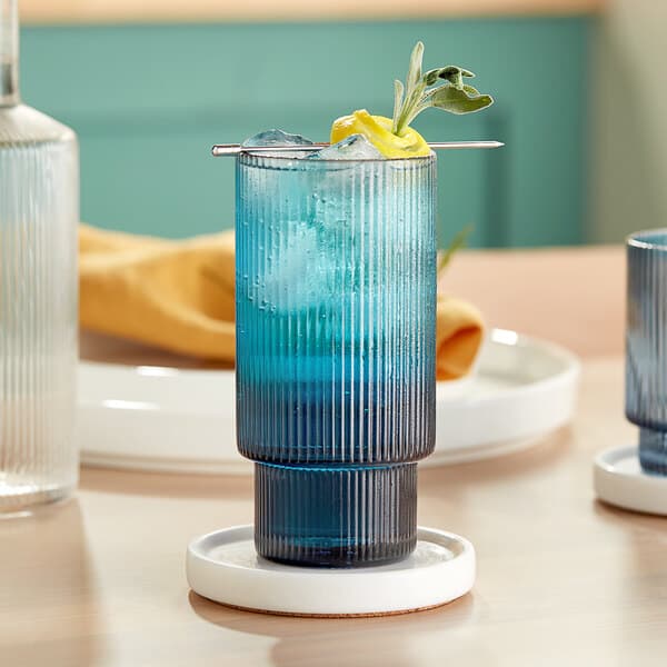 A blue drink in an Acopa Lore highball glass with a lemon wedge and a straw.