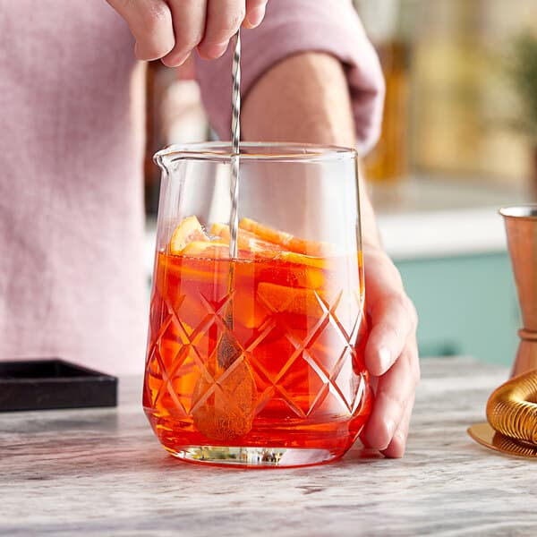 A person stirring an orange cocktail in an Acopa bold diamond cut mixing glass.