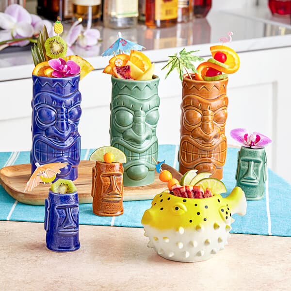 A collection of colorful Acopa ceramic tiki shot glasses filled with fruit.