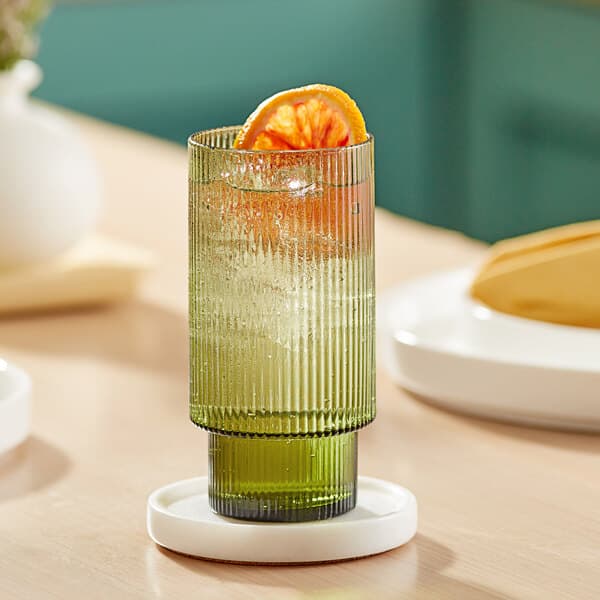 A close-up of a green Acopa Lore highball glass with a slice of orange in it.