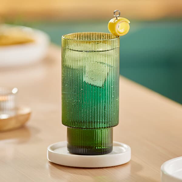 A green highball glass with a drink and lemon wedge on top.
