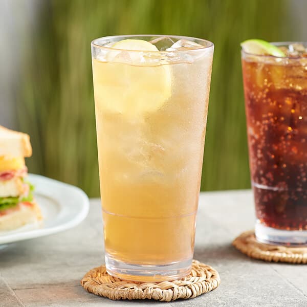 A table with a sandwich and two Acopa Endure Tritan plastic stackable cooler glasses filled with ice tea and water with lemon slices.